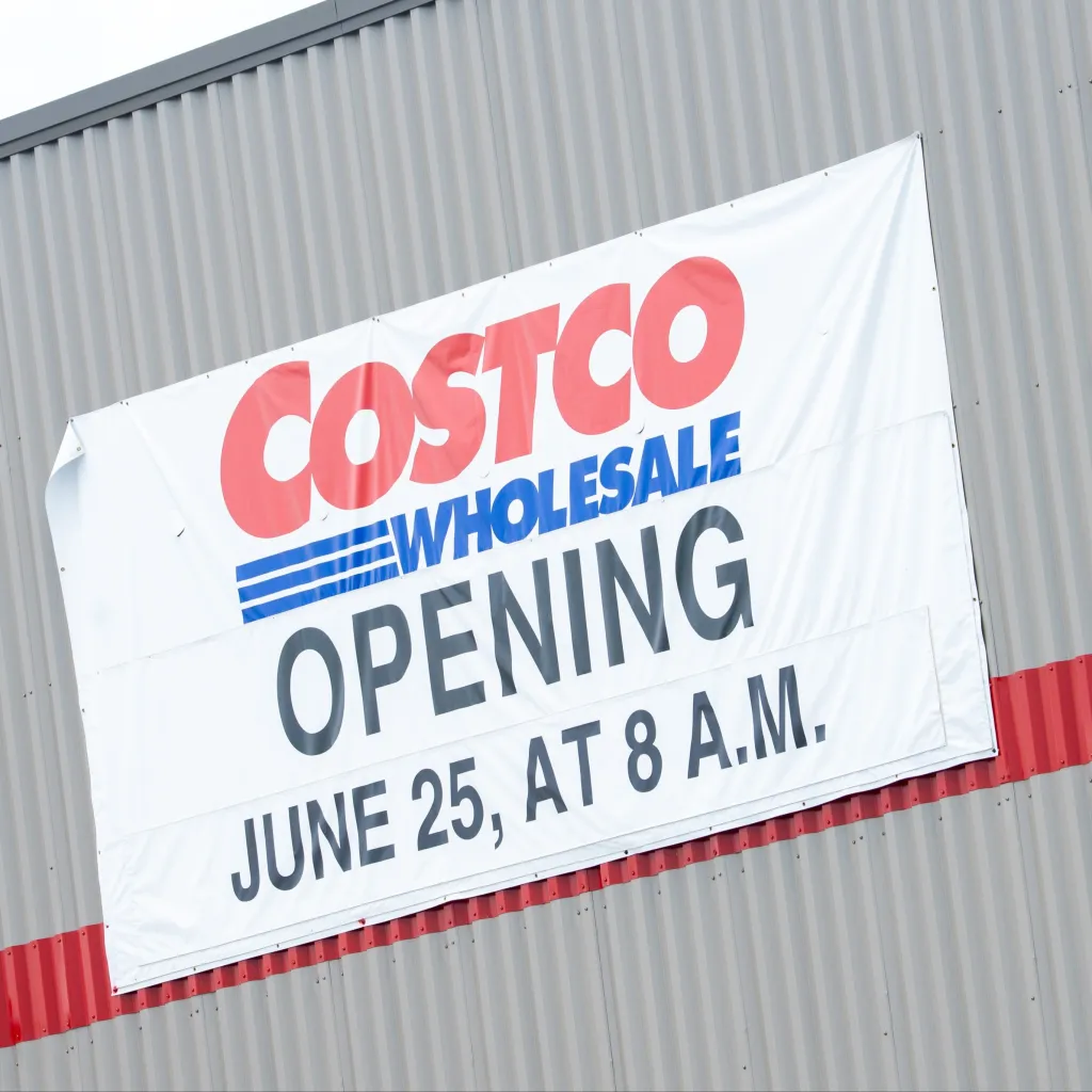A banner on the side of a Costco building announcing its opening on June 25th at 8 AM.