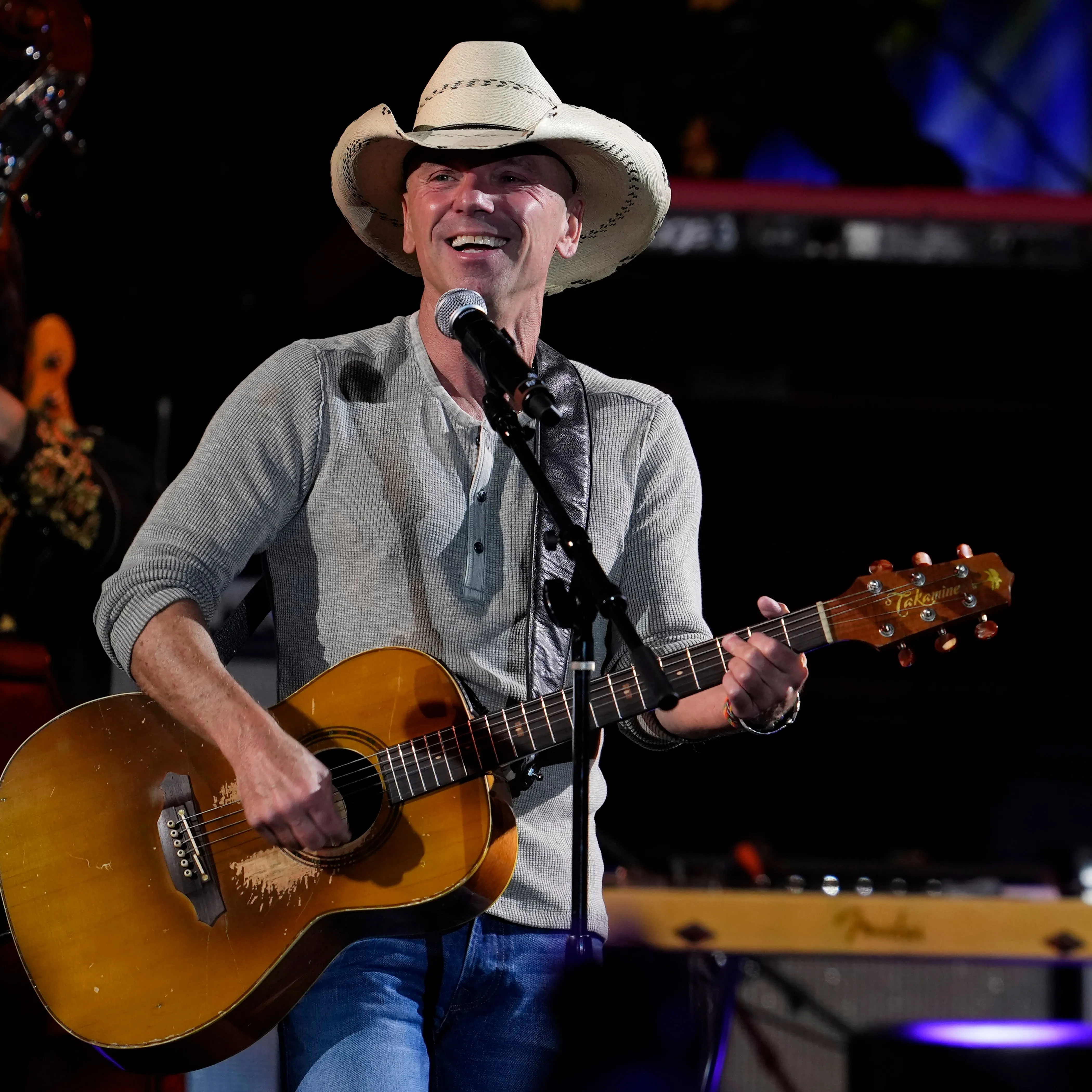 Kenny Chesney performing on stage with an acoustic guitar and microphone.