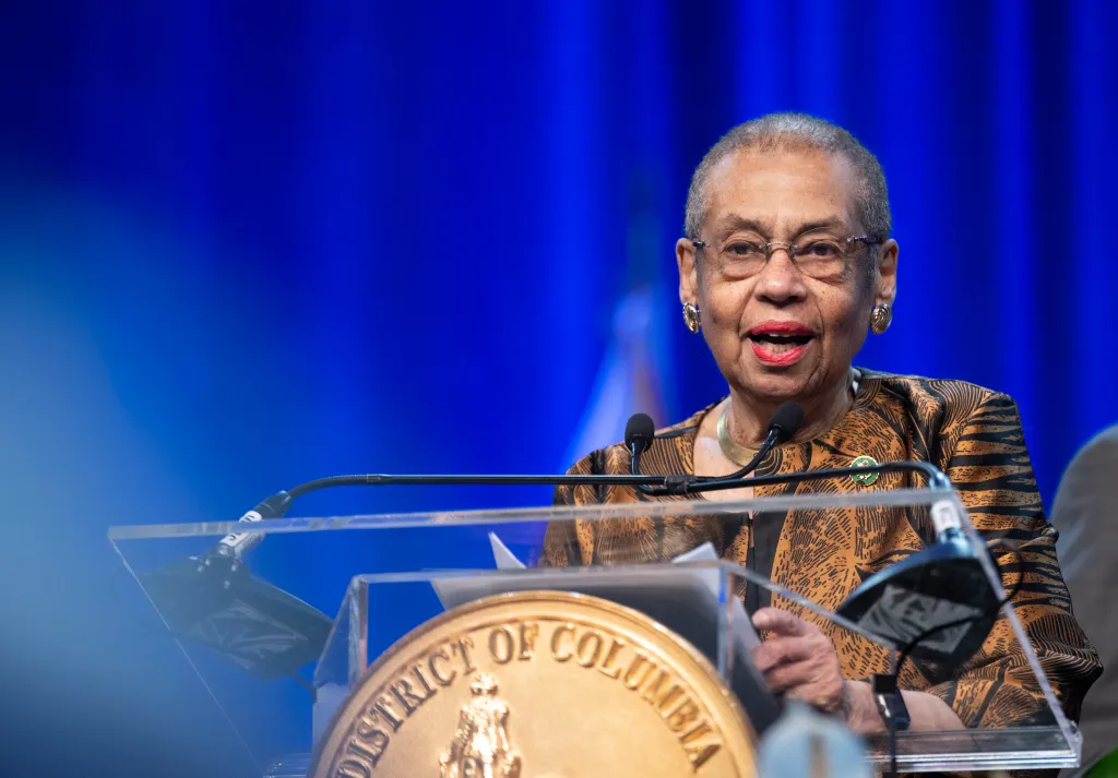 Congresswoman Eleanor Holmes Norton speaking at a podium with a gold seal of the District of Columbia.