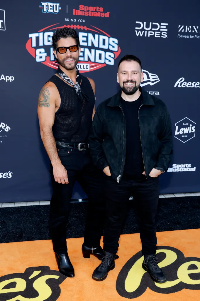 Dan Smyers and Shay Mooney of Dan + Shay pose for a photo on an orange carpet with various sponsor logos in the background.