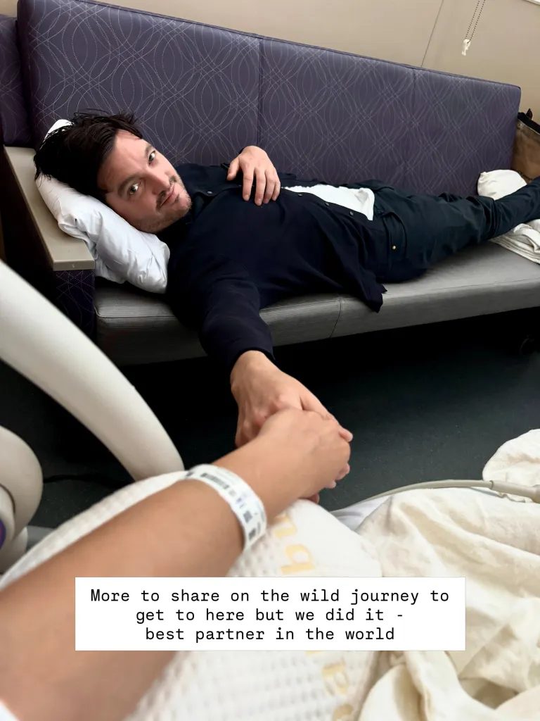 A man lying on a bench, holding hands with someone in the foreground who has a hospital band on their wrist.