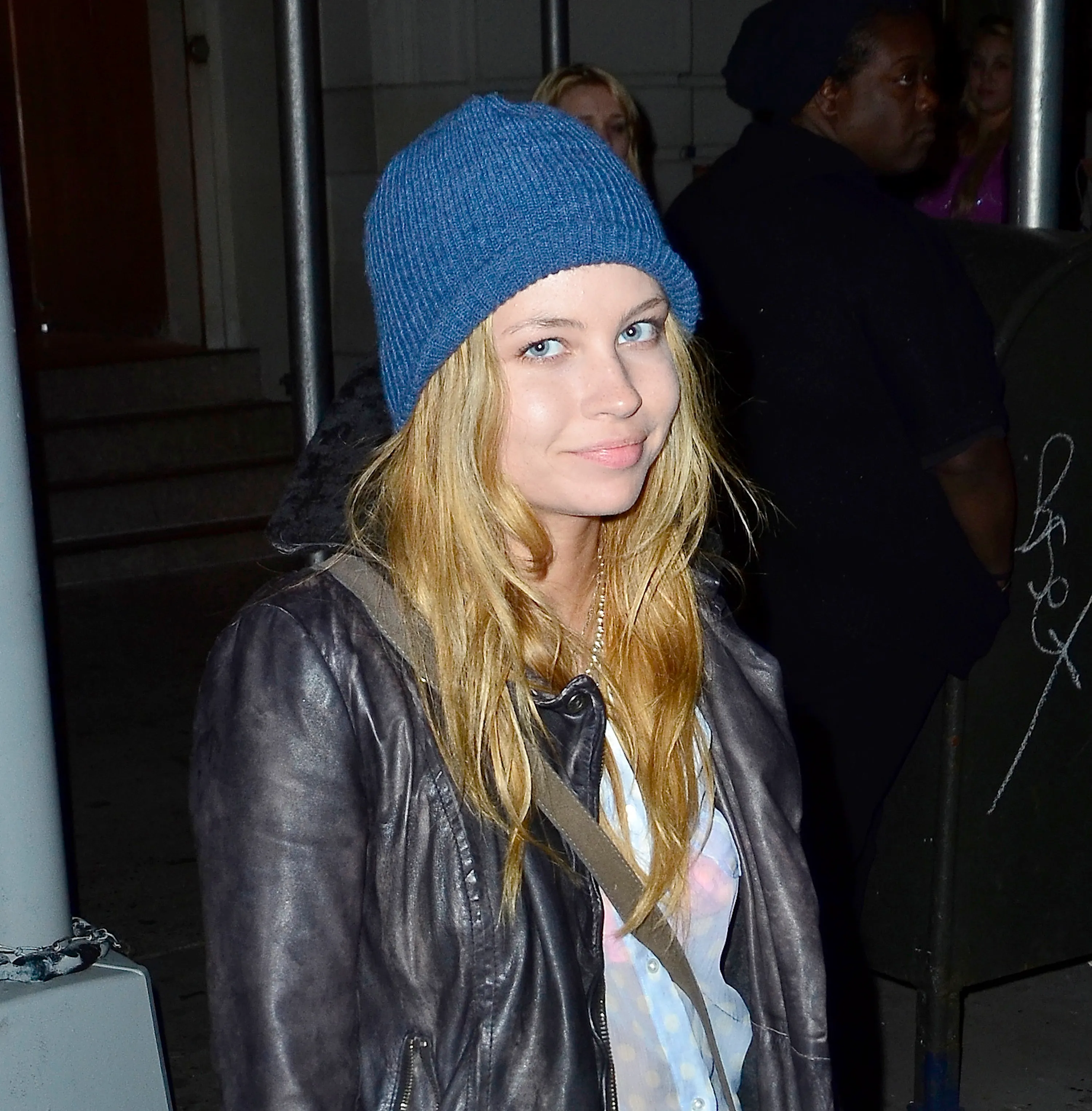 Daveigh Chase, wearing a blue beanie and black leather jacket, gazes directly at the viewer.