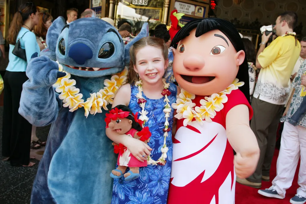 Daveigh Chase, the voice of Lilo, smiling between costumed characters Stitch and Lilo at the premiere of 