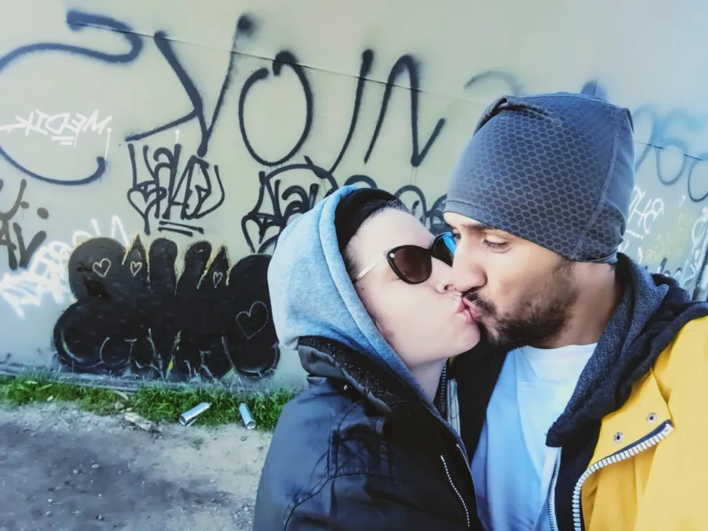 A man and woman kissing in front of a graffiti-covered wall.