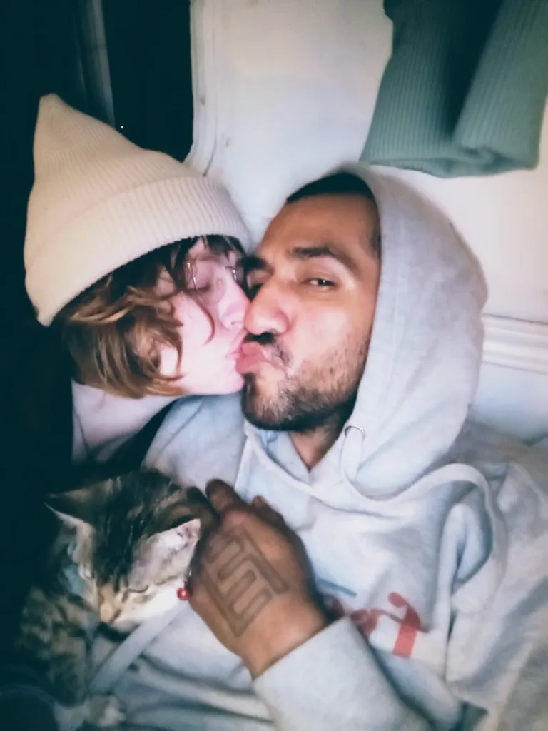 Daveigh Chase kissing Roy Hernandez on the cheek while a cat sits near them.