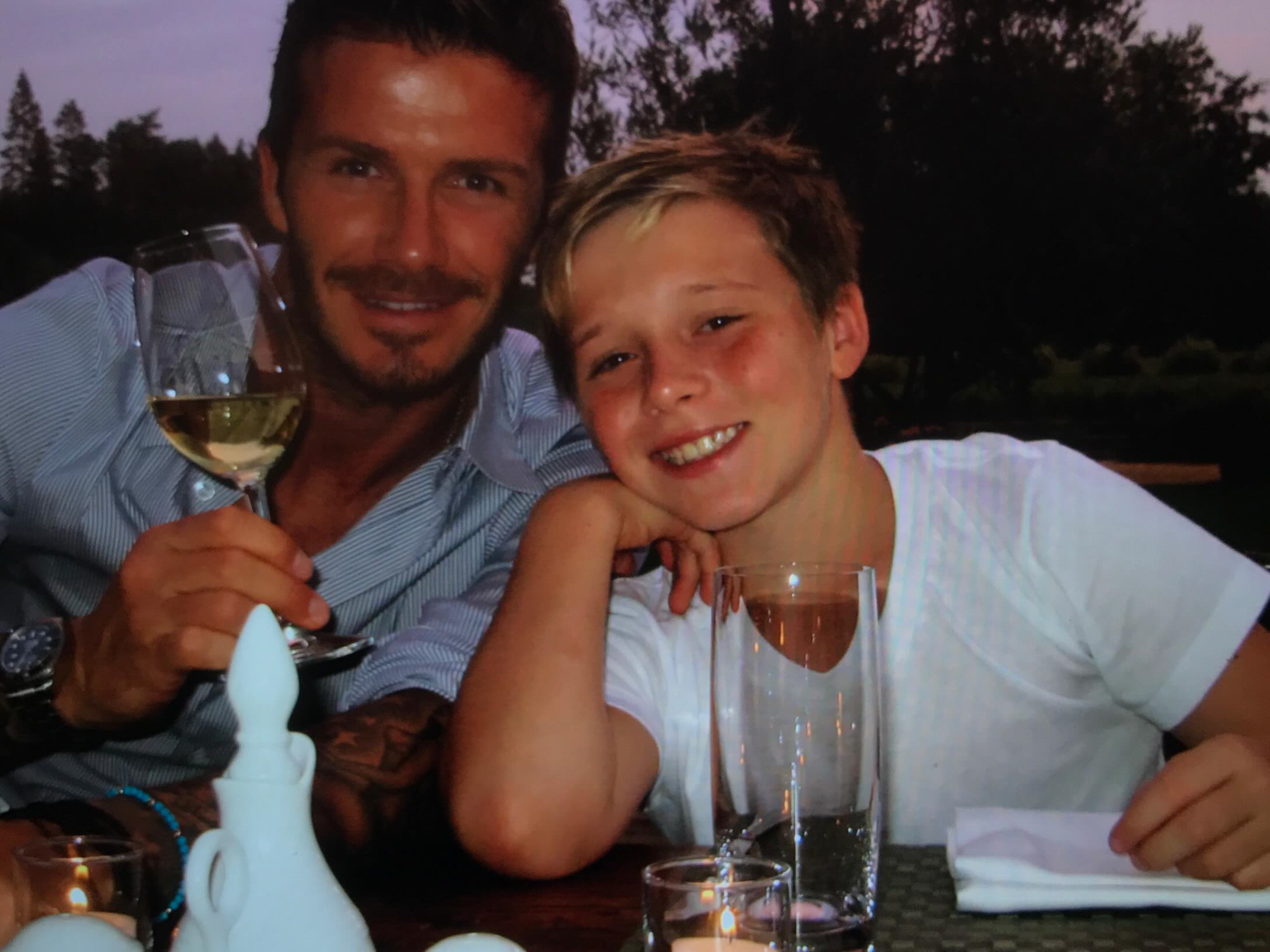 David Beckham and his son Brooklyn Beckham at a table with drinks and candles.