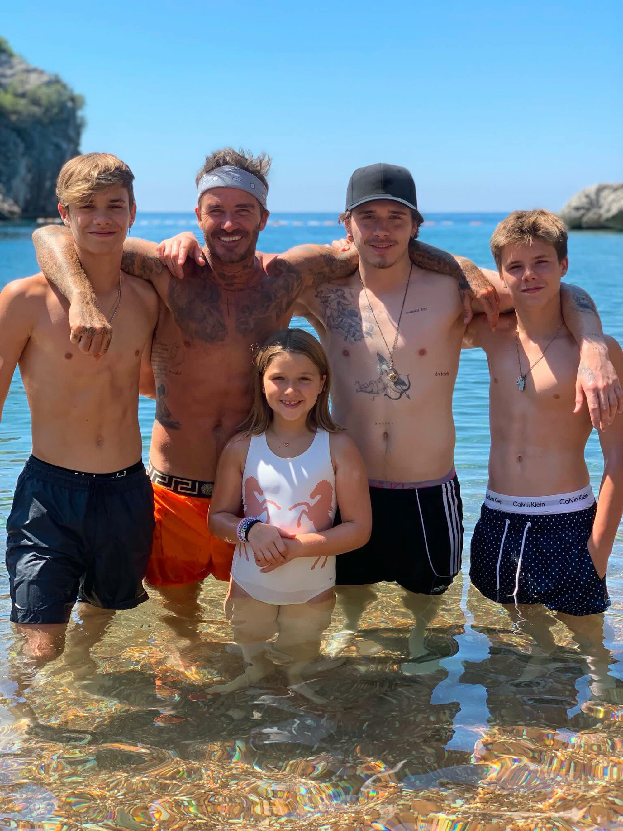 David Beckham and four children standing in clear ocean water.
