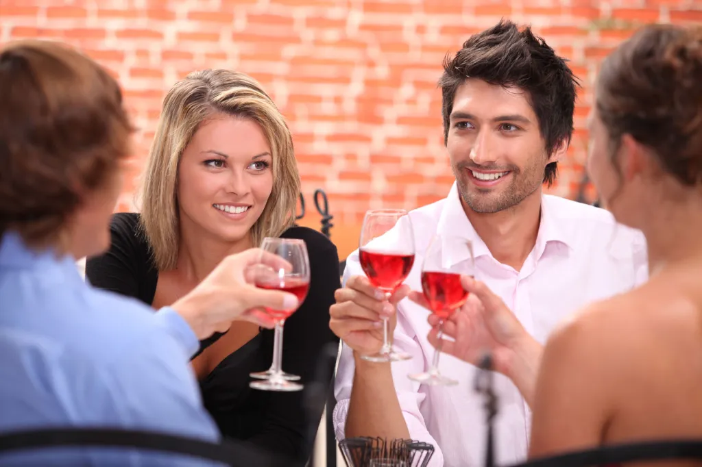 Two couples toasting wine glasses at a restaurant.