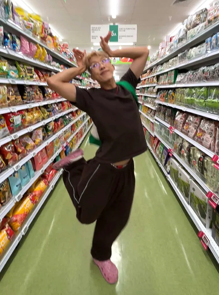 Person with arms raised posing for a photo in a grocery aisle.