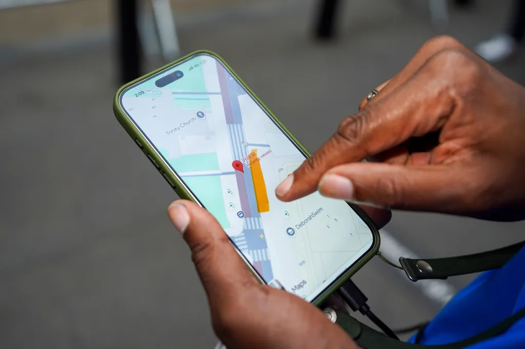 A person's hands holding a cell phone displaying a map of Trinity Church and Wall Street, with a desired spot highlighted.