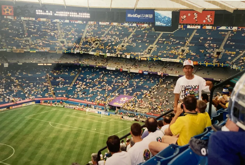 Spectators in blue stadium seats watch a World Cup 1994 game between Brazil and Sweden at the Pontiac Silverdome, with advertisements and banners visible.