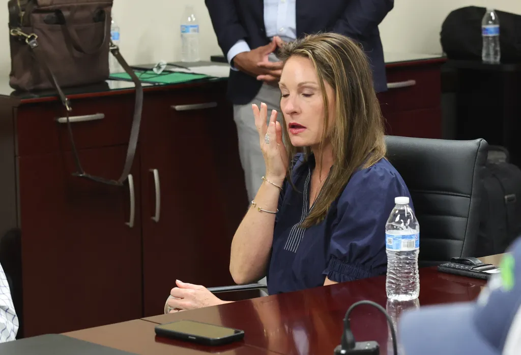 Christie Mullin in a navy top, seated at a desk, touching her face.