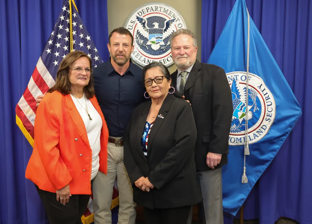 DHS Secretary Markwayne Mullin, Agnes Gibboney, Angie Morfin, and Don Rosenberg pose in front of US and DHS flags.