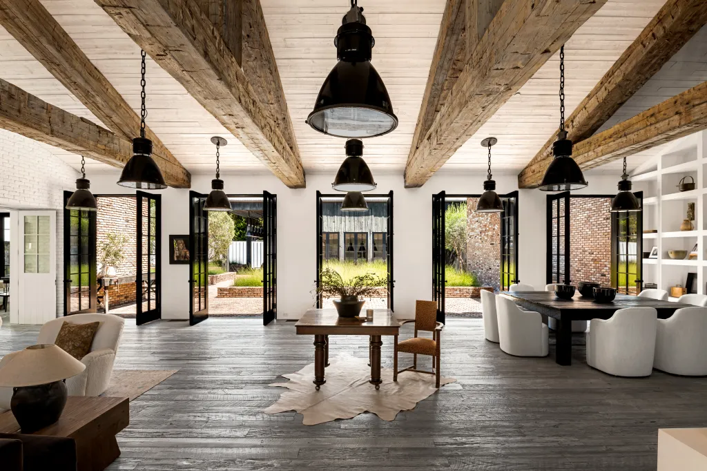 Large open-concept living space with wooden beams, dark hardwood floors, two dining areas, and multiple French doors leading to a courtyard.