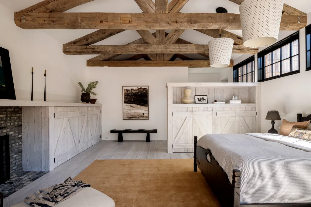 A rustic bedroom with exposed wooden beams, barn-door style cabinetry, and a dark wooden bed frame with a striped duvet.