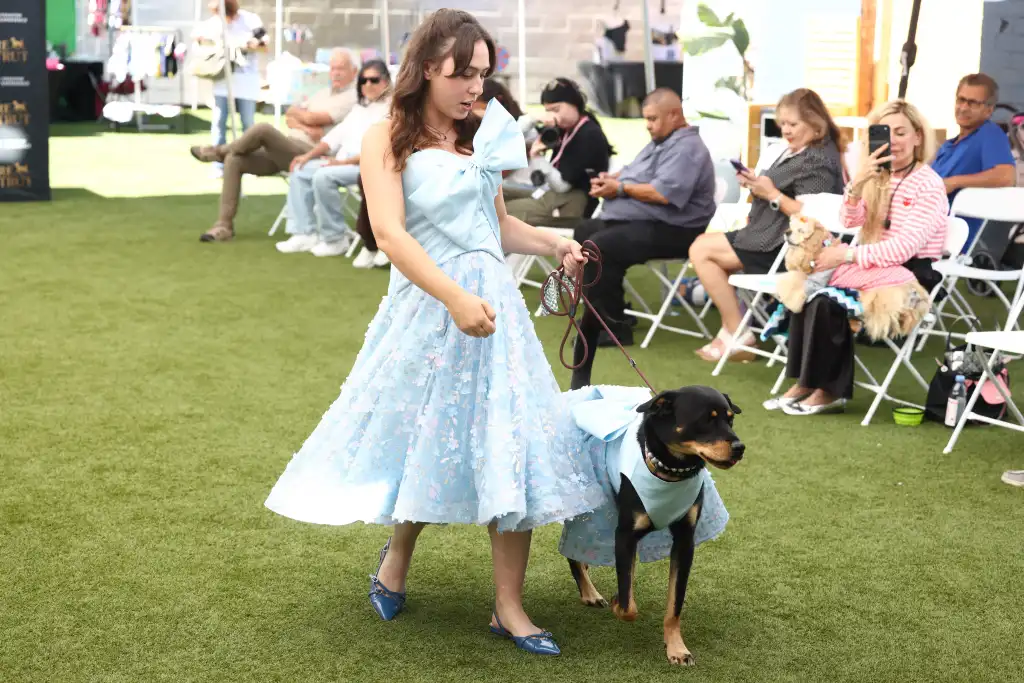 A woman and her dog wearing matching blue outfits walk a fashion runway.