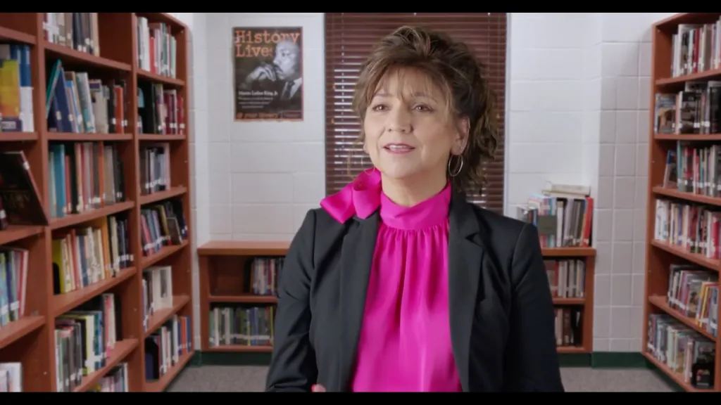 Dr. Rubylinda Zickafoose, wearing a black blazer and a fuchsia blouse, stands in a library.