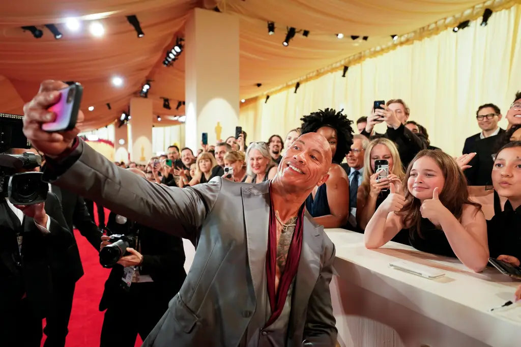 Dwayne Johnson takes a selfie with fans on the red carpet at the 96th Oscars.