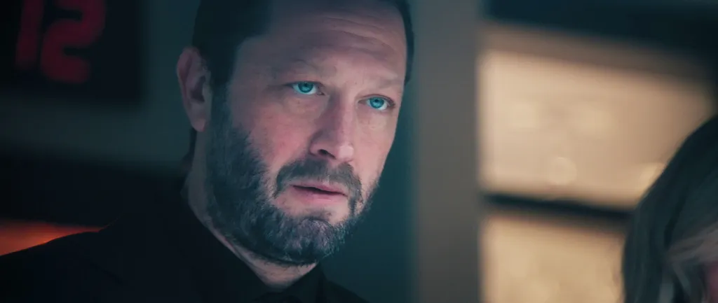 Ebon Moss-Bachrach as Richie Jerimovich with glowing blue eyes, looking serious in a dark room.