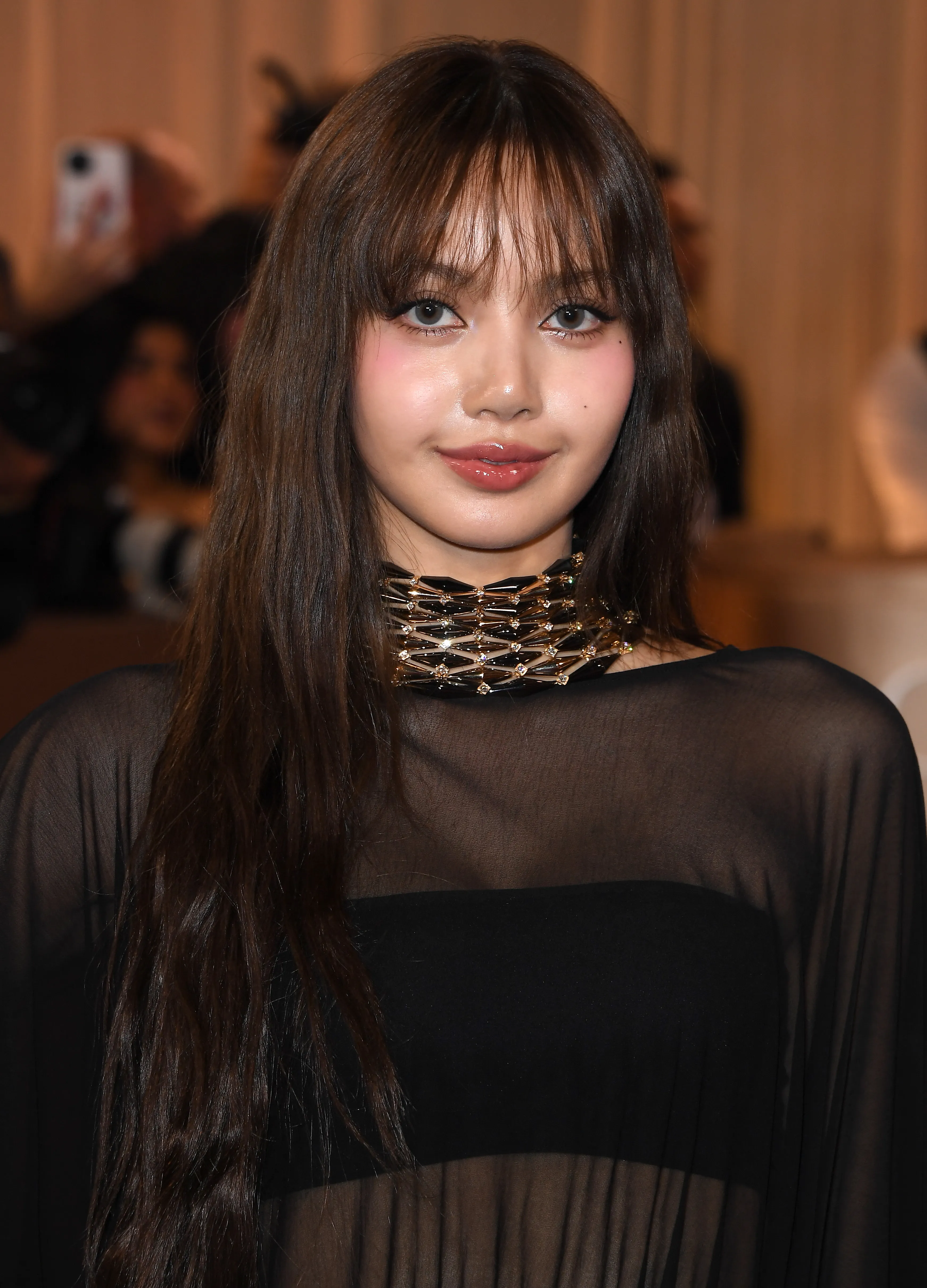 Lalisa Manobal with long brown hair, bangs, and a black and gold choker, smiling at the 83rd Annual Golden Globe Awards.