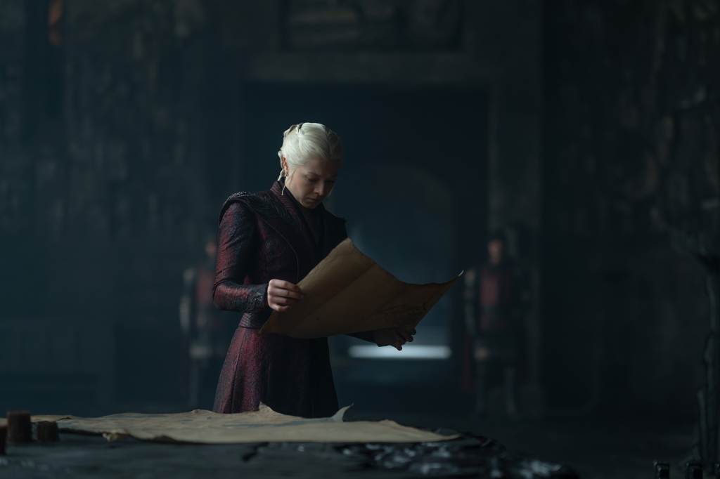Emma D'Arcy as Rhaenyra Targaryen from House of the Dragon, wearing a dark red dress and looking down at a scroll.