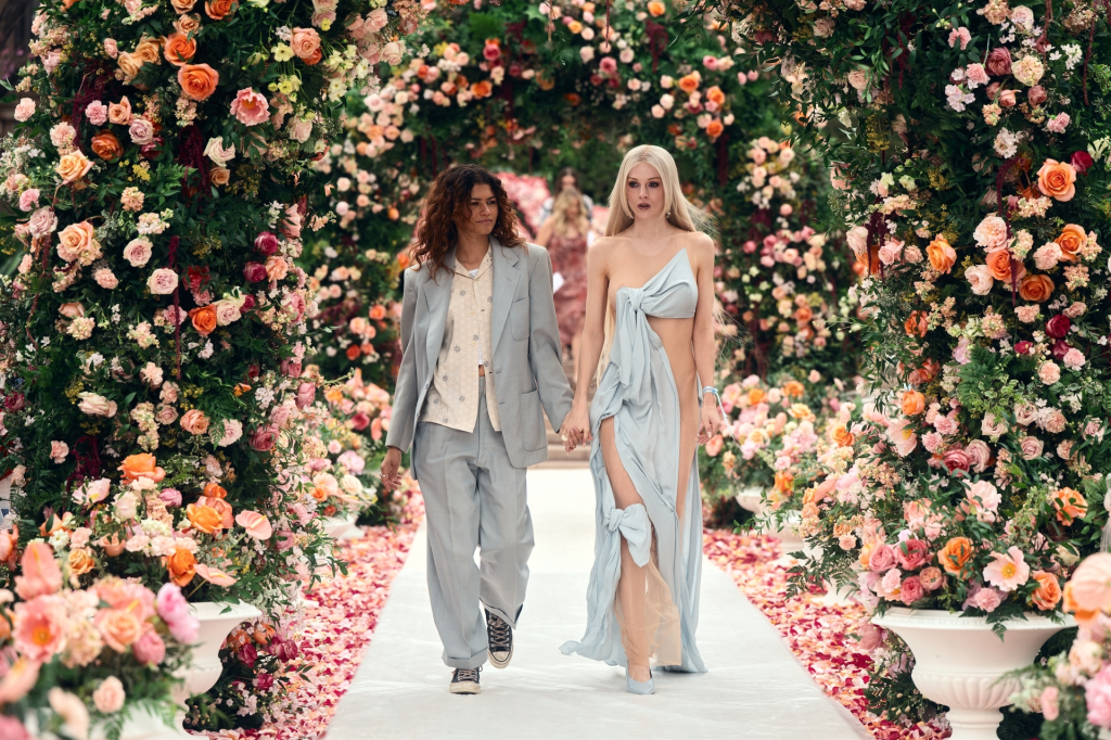 Zendaya and Hunter Schafer holding hands on a flower-covered runway for Euphoria.