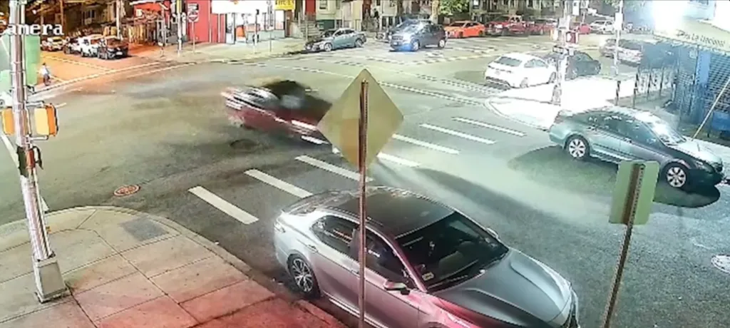 Surveillance footage of a red car in a hit-and-run crash at an intersection.