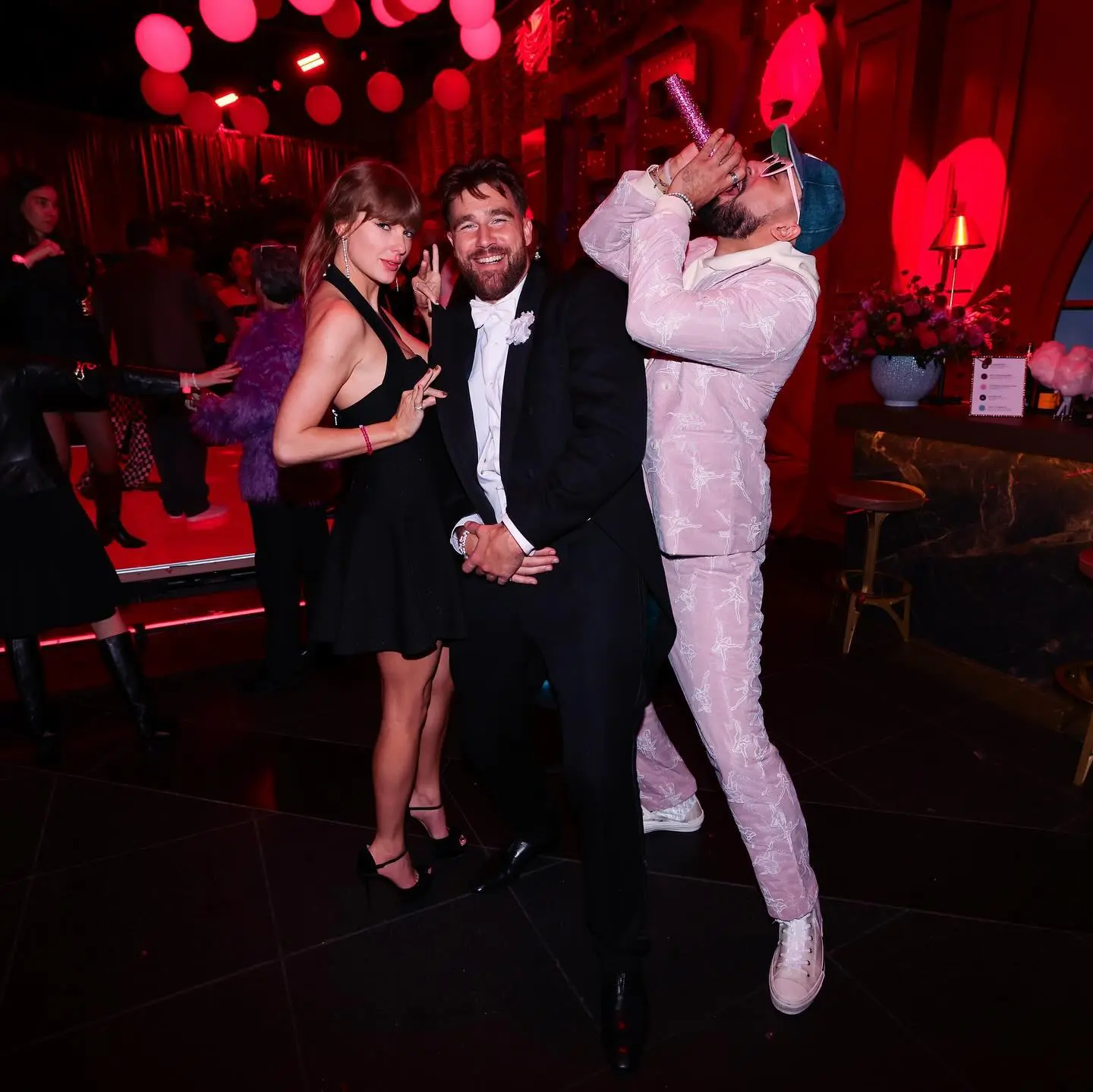 Taylor Swift and Travis Kelce posing for a photo with a third person who is blowing a party horn.
