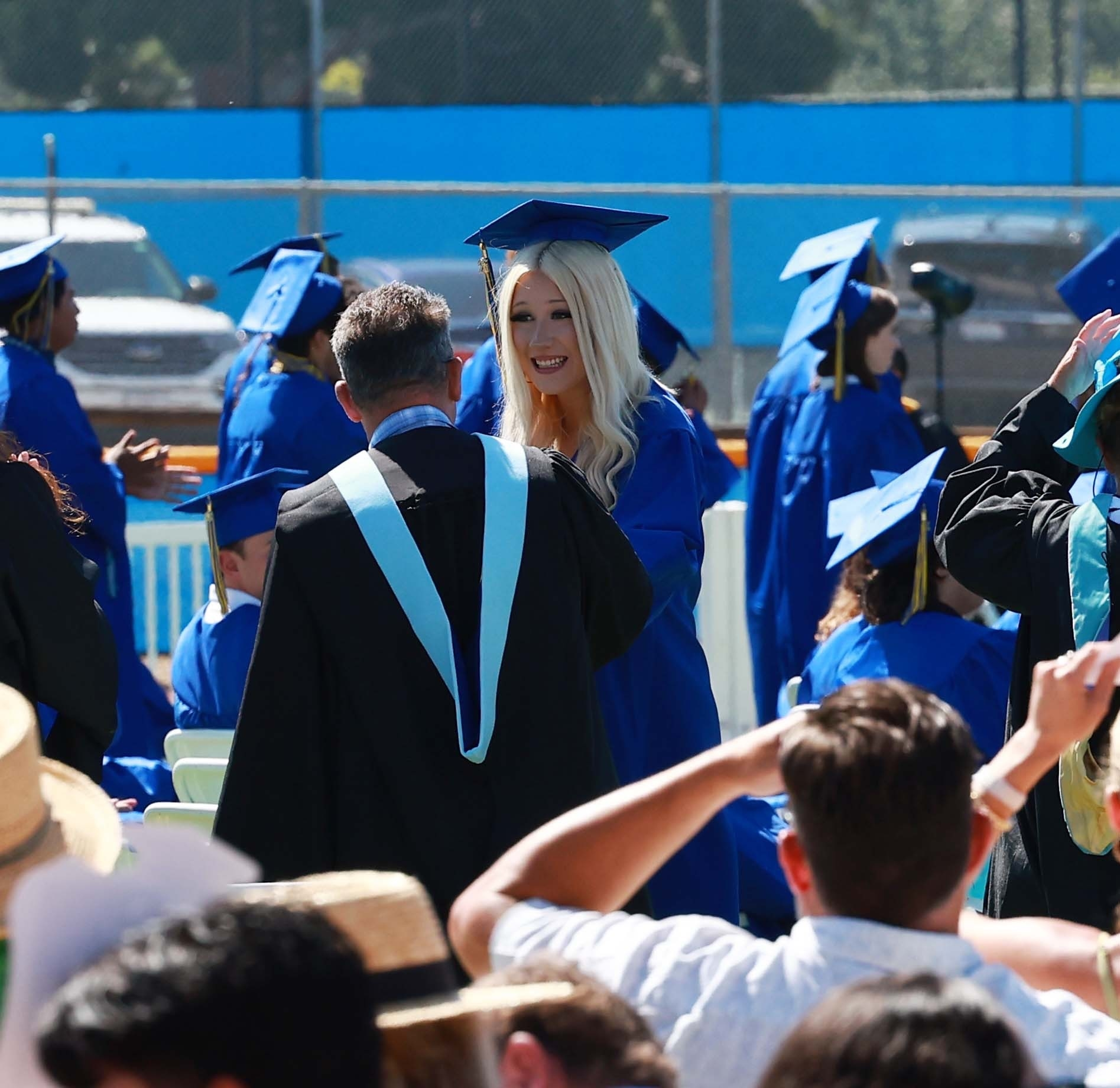 Stella McDermott in a blue graduation gown and cap, smiling and talking to a man in a black gown with a light blue stole.