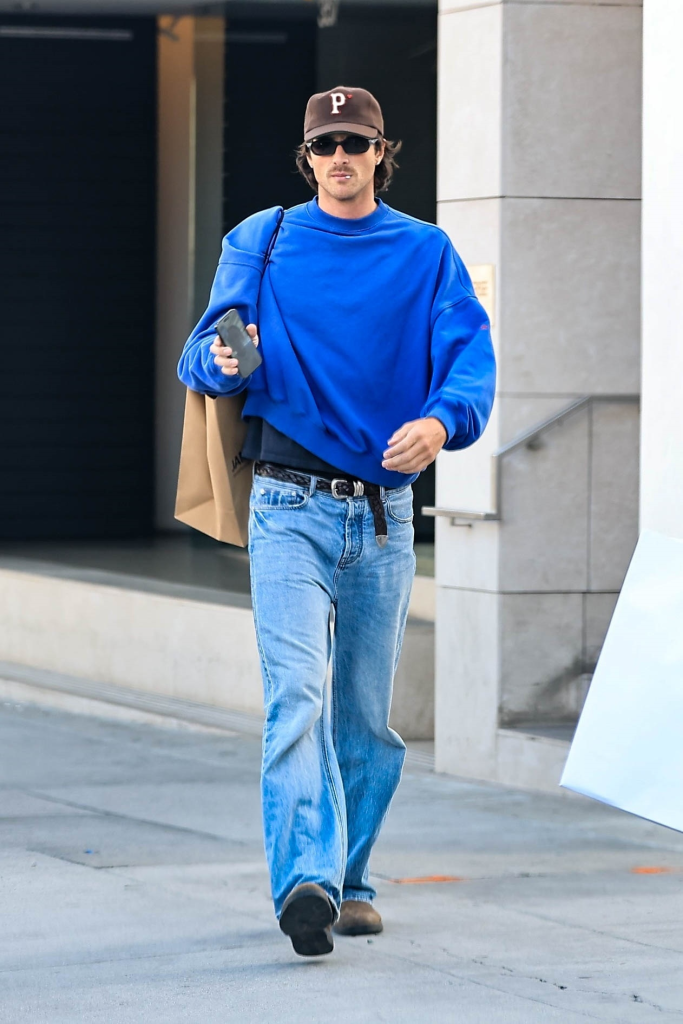 Actor Jacob Elordi wearing a blue shirt, blue jeans, and a baseball cap while shopping.