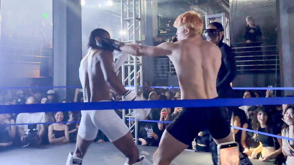 Knox Jolie-Pitt in an exhibition fight, striking an opponent in a boxing ring.