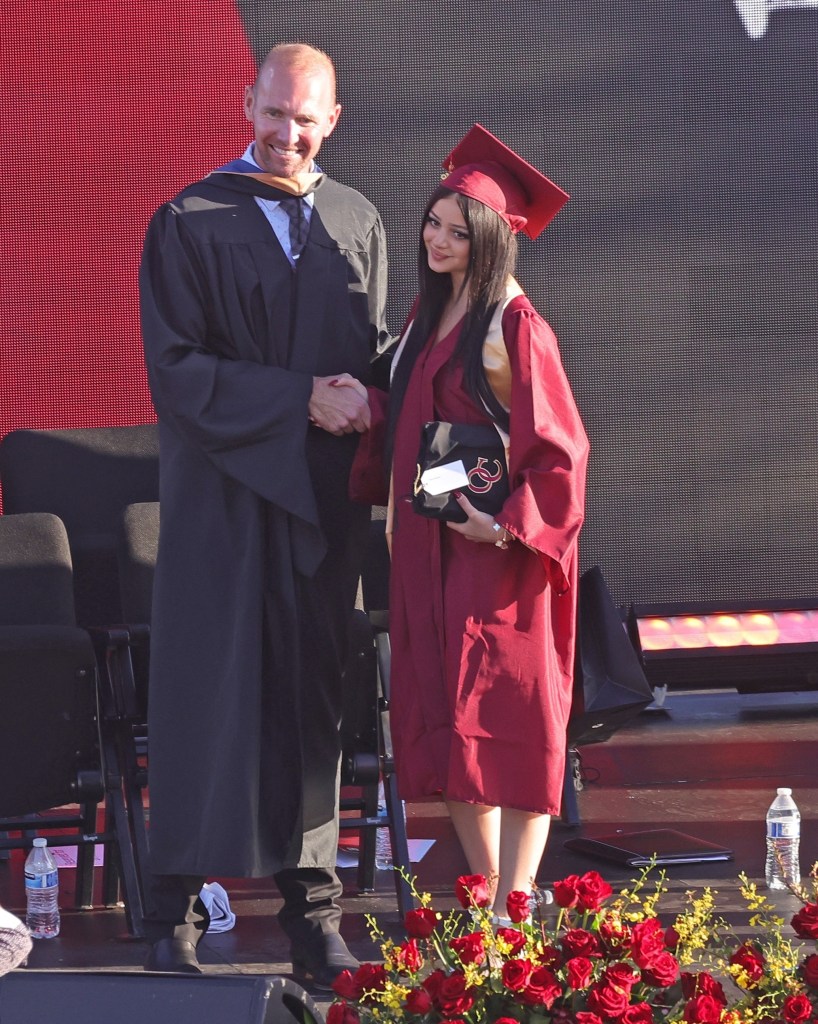 Kate Richie Madden in a red graduation gown shaking hands with a man in a black graduation gown.