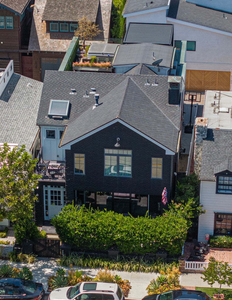 Aerial view of Tarek El Moussa and Heather Rae El Moussa's dark gray house with a small balcony and American flag hanging by the entrance, surrounded by other Newport Beach homes.