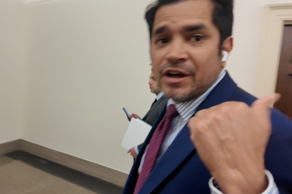 Congressman Jimmy Gomez walking and gesturing with his thumb, looking at the camera.