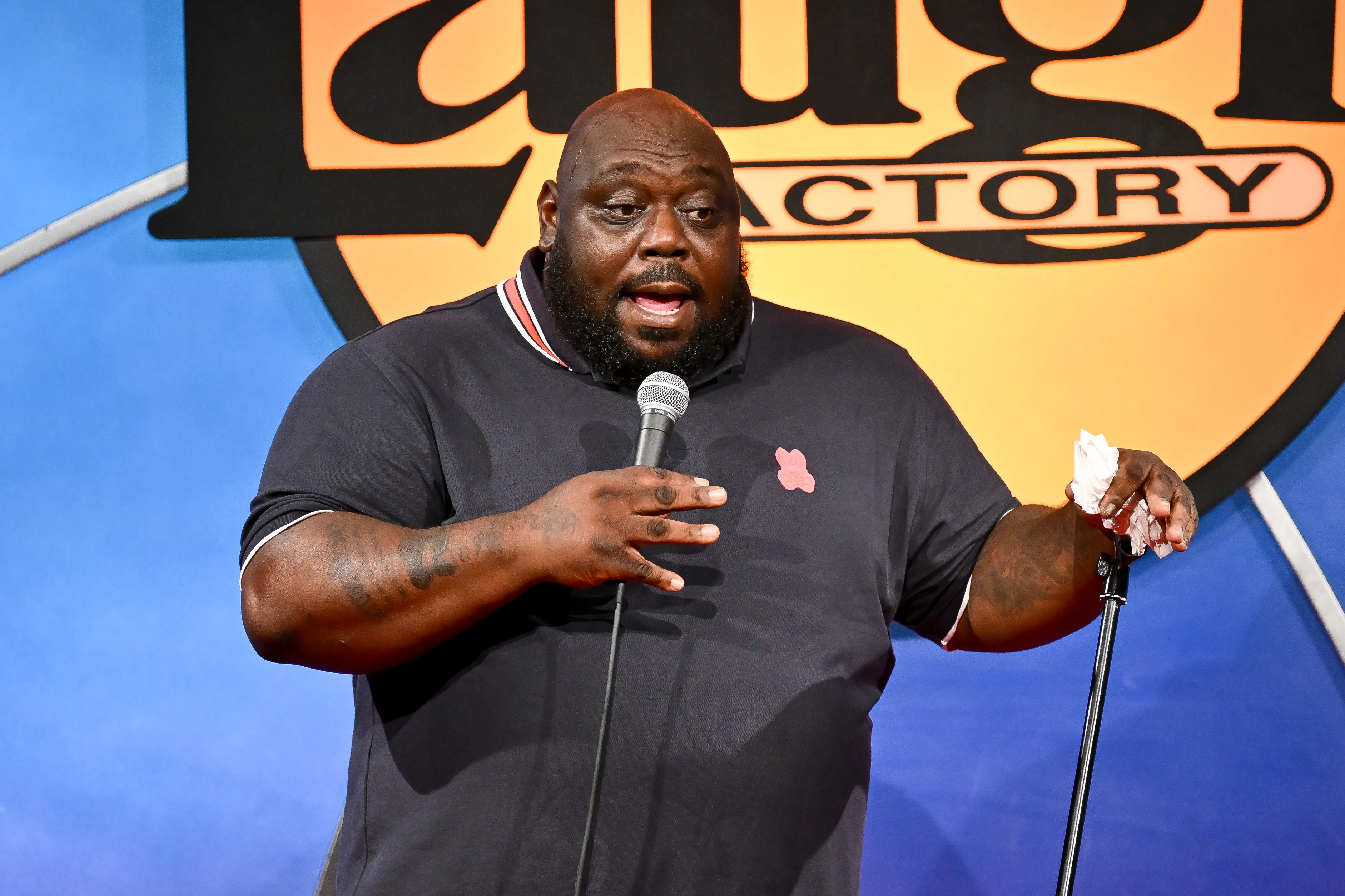 Faizon Love speaking into a microphone onstage at the Laugh Factory.