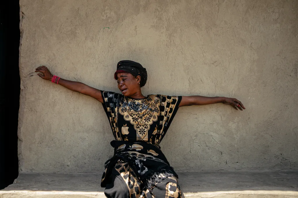 A woman, identified as a family member of a suspected Ebola victim, cries with her arms outstretched against a beige wall in Bunia, Democratic Republic of Congo.