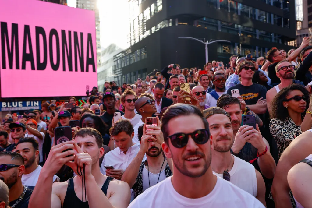 Fans dancing at Madonna's pop-up concert with a large pink 