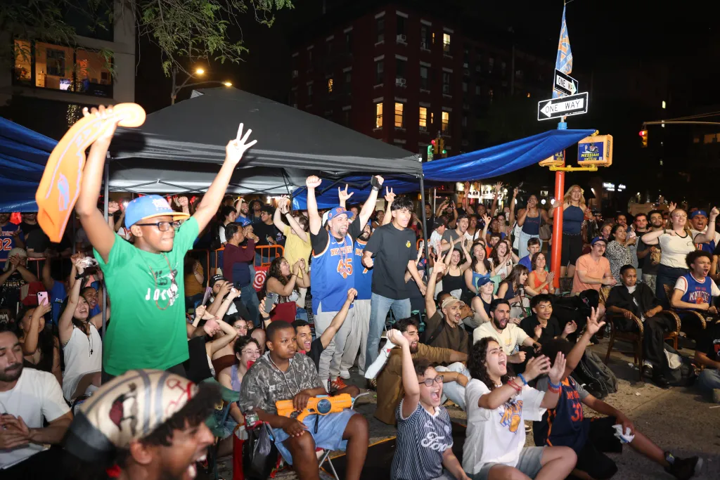 Fans cheer while watching the NY Knicks game 4 of the NBA Finals on an outdoor screen.