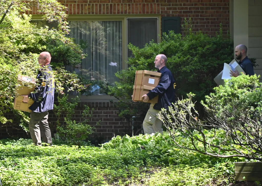 Three FBI officers carry evidence boxes and documents from John R. Bolton's home.