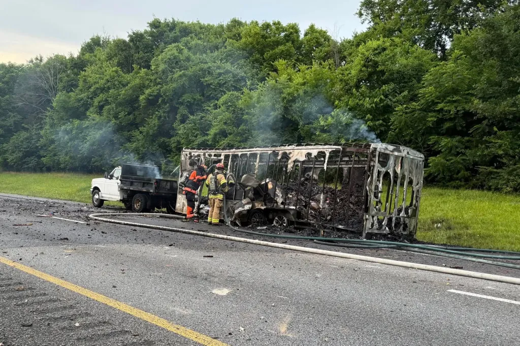 Firefighters investigating a burned-out trailer that had been carrying fireworks, with a pickup truck in the background.