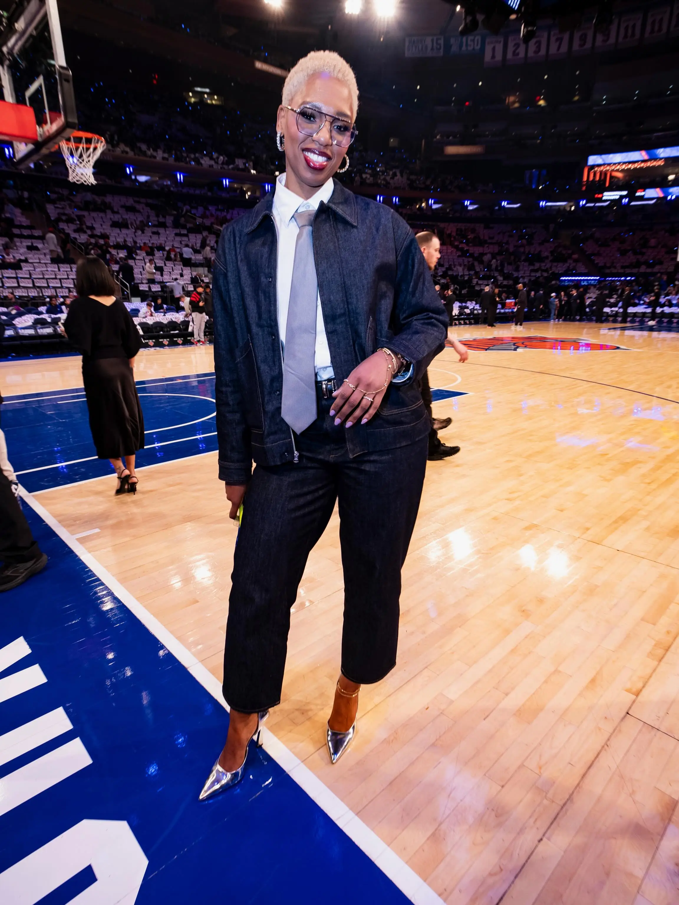 Monica McNutt in a denim suit with a white shirt and gray tie, standing on a basketball court.