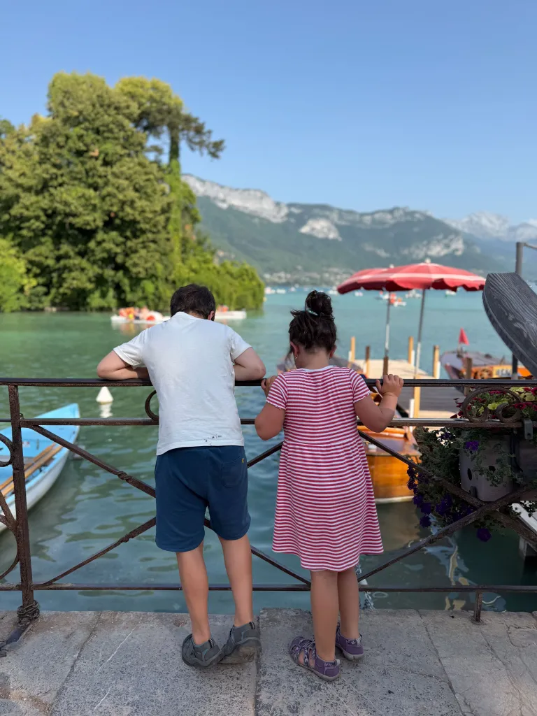 Two children viewing a lake with boats and mountains.