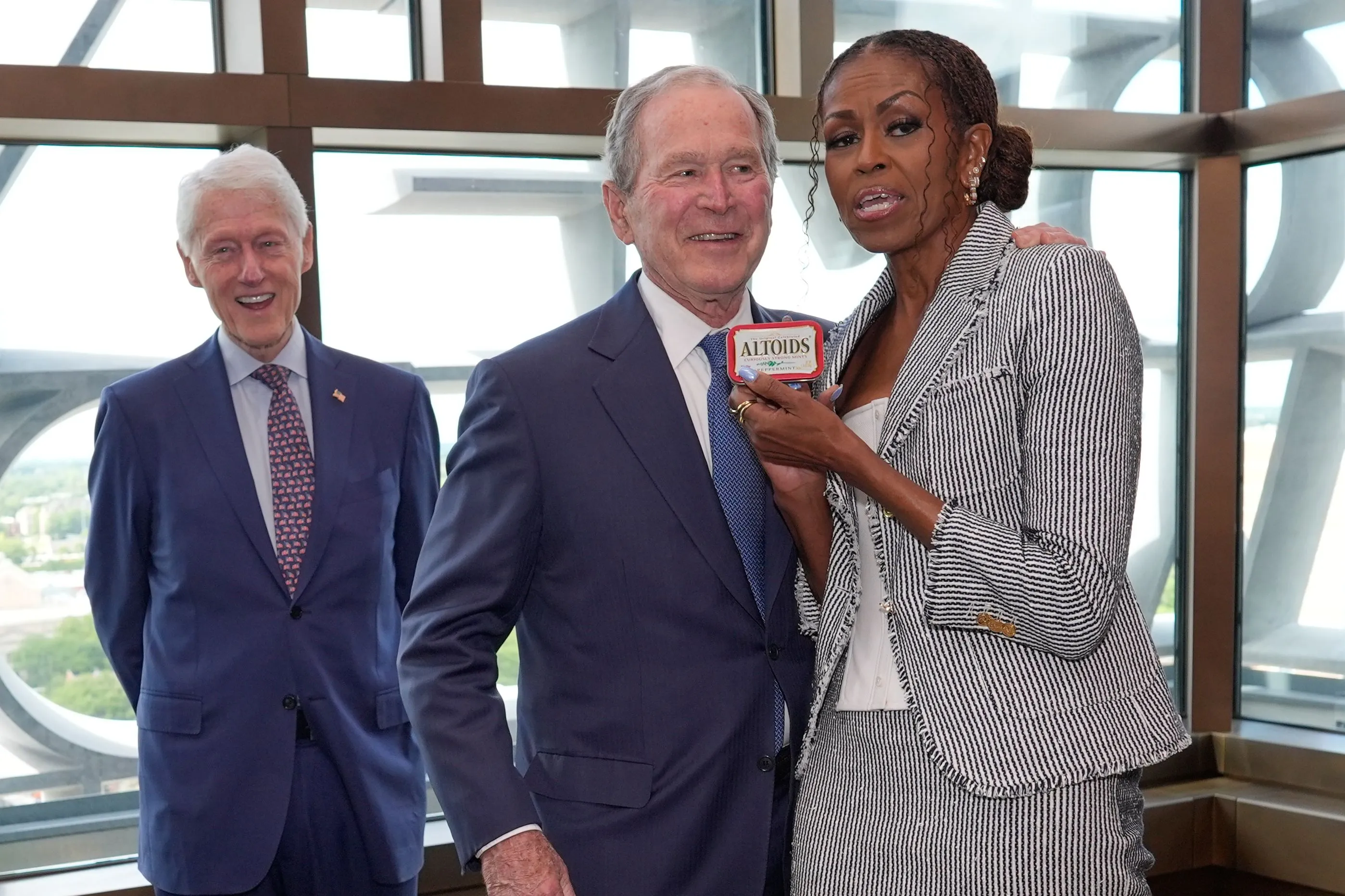 Former President George W. Bush gives former first lady Michelle Obama mints, while former President Bill Clinton smiles in the background, at the Obama Center dedication.