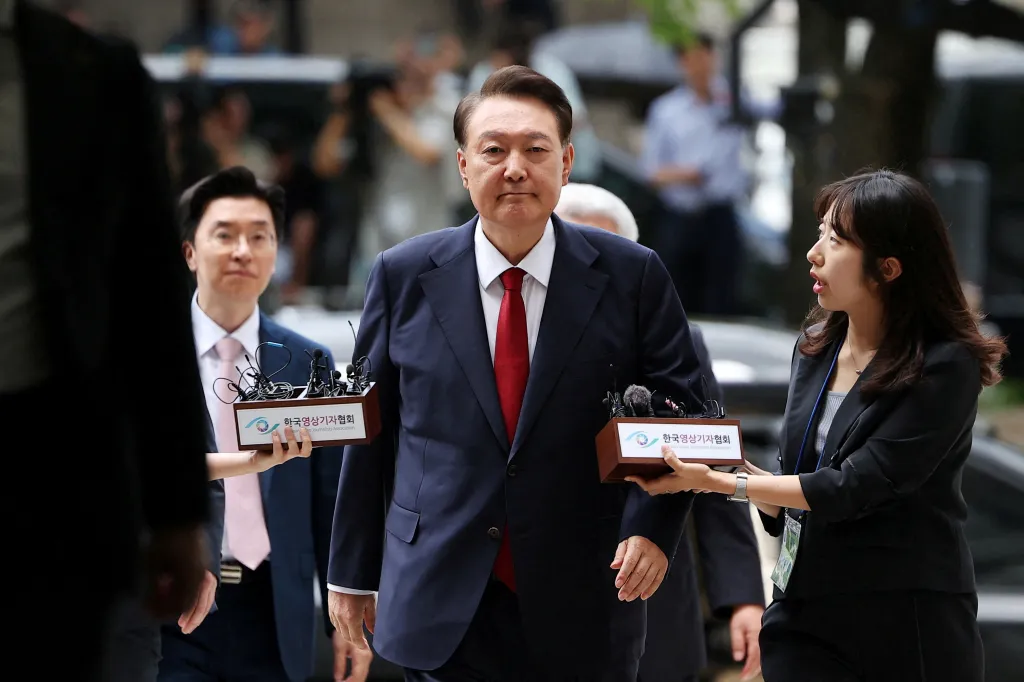 Former South Korean President Yoon Suk Yeol walks through a crowd as two people hold boxes containing microphones with the text 