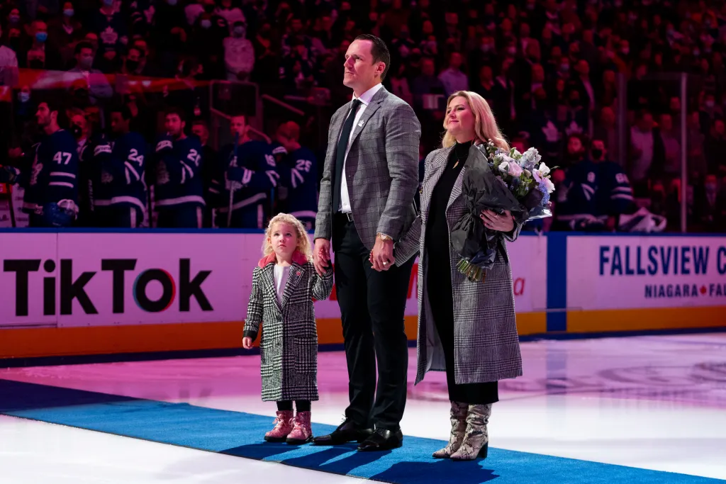 Dion Phaneuf, his daughter, and his wife Elisha Cuthbert stand on an ice rink during a ceremony.
