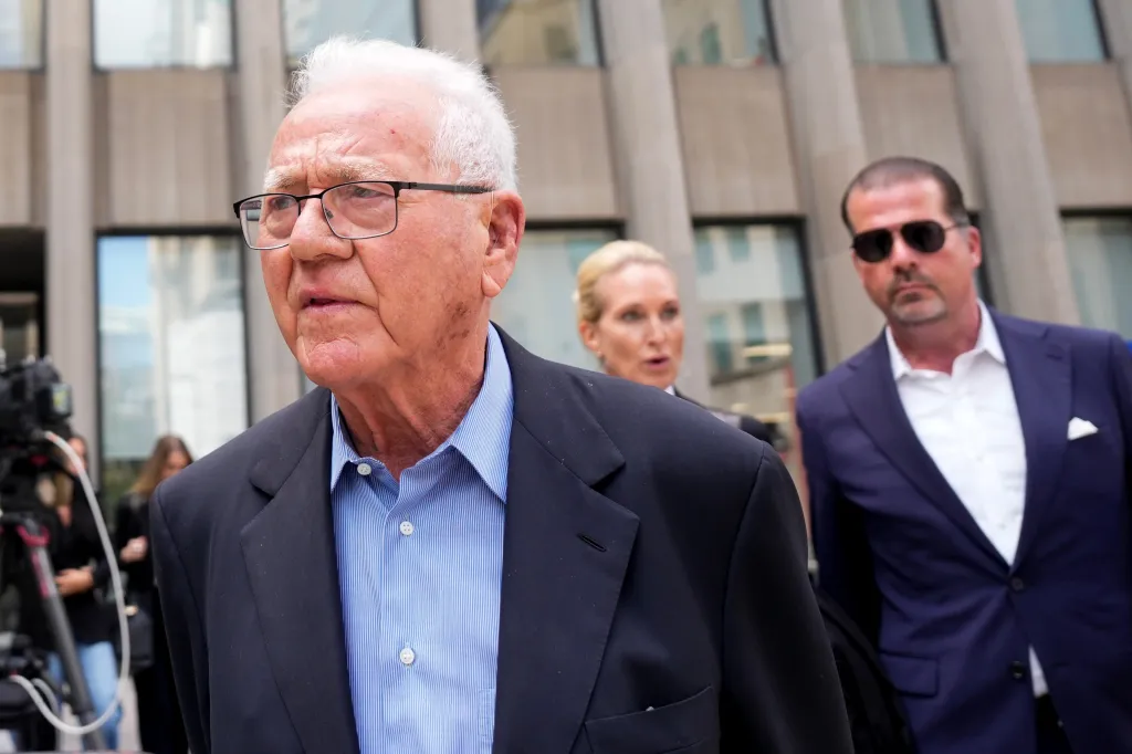 Frank Stronach, wearing glasses and a suit, leaving a Toronto court with two other individuals.