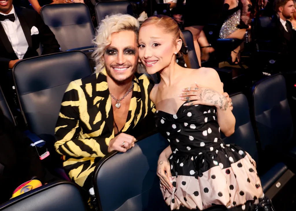 Frankie Grande, in a yellow and black striped suit, and Ariana Grande, in a black and white polka dot dress, smiling together at the MTV Video Music Awards 2025.