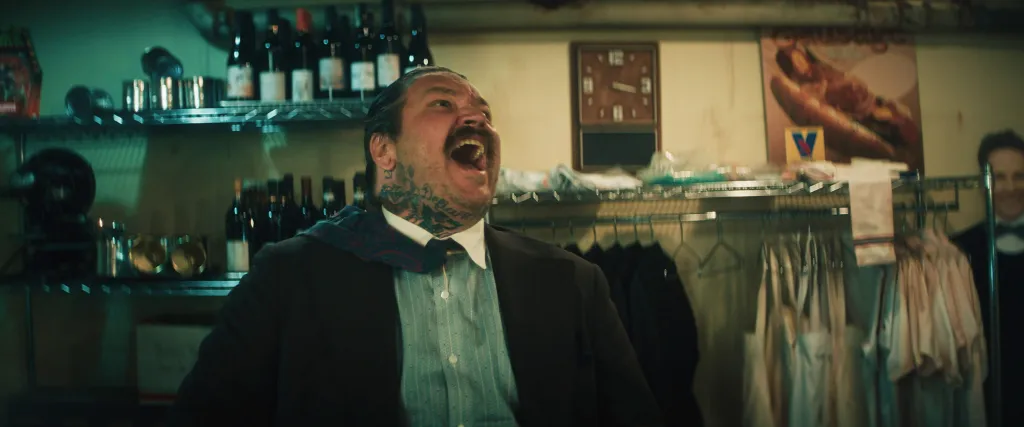 Neil Fak, a man with a mustache and neck tattoos, laughs loudly in a restaurant storage room.