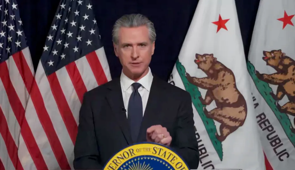 Gavin Newsom, Governor of California, speaks at a podium with American and Californian flags behind him.