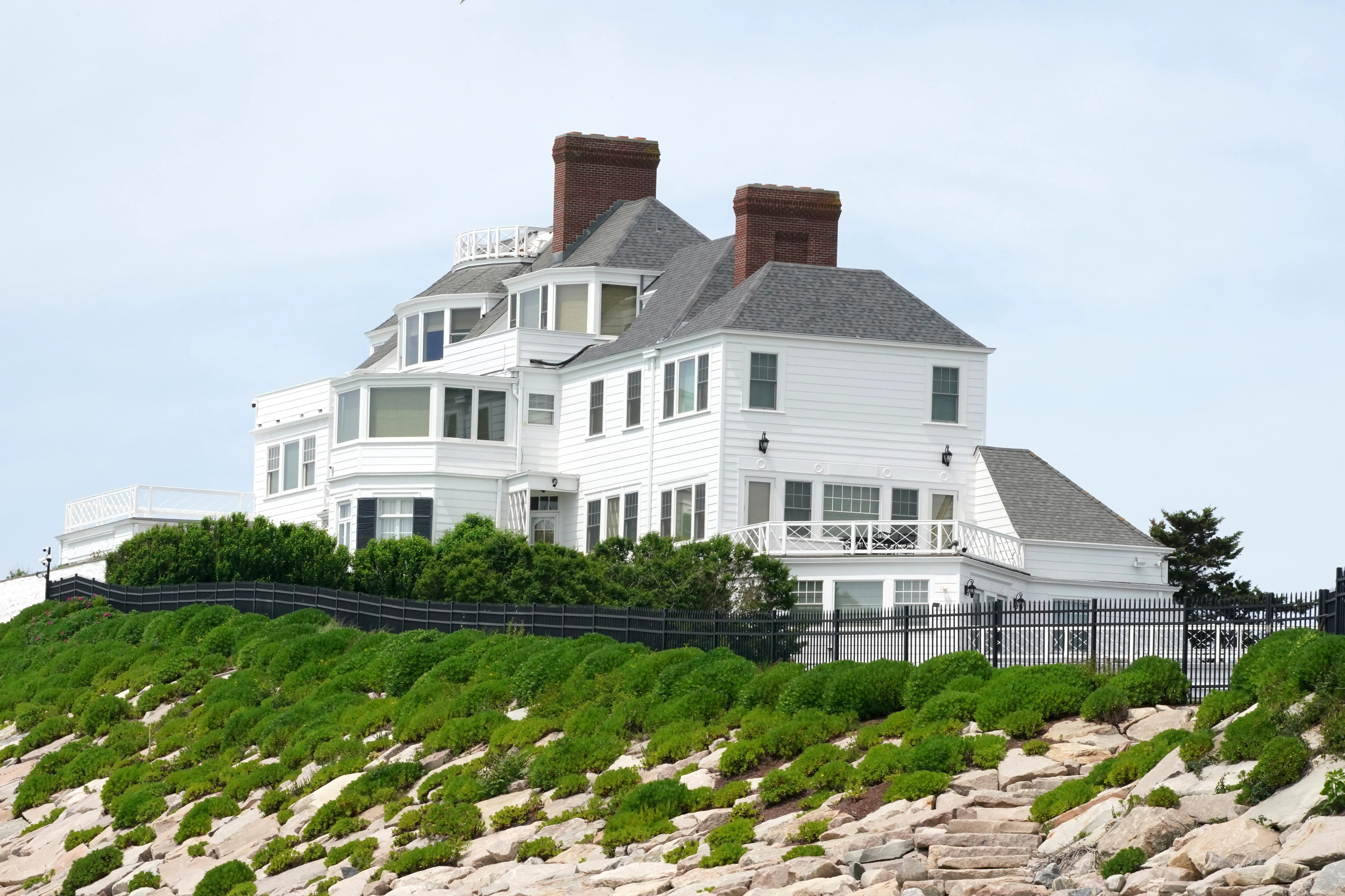 Taylor Swift's home at 16 Bluff Avenue in Westerly, Rhode Island, visible above a landscaped hill with a black fence.